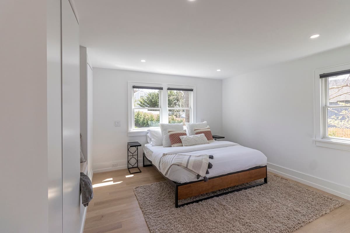 Bright guest bedroom with pristine white walls, natural light, and decorative pillows