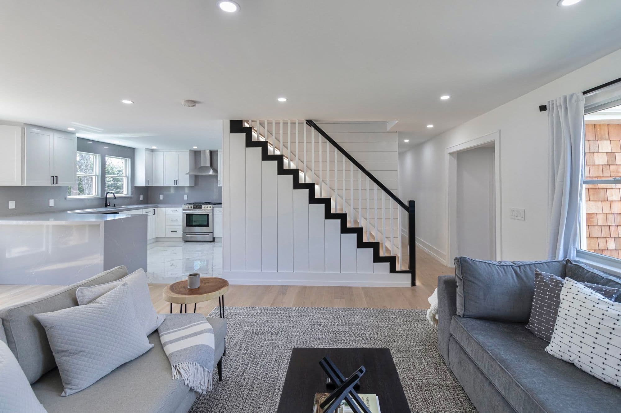 Open living area with gray sofas, white shiplap staircase, and cedar shingle exterior accents
