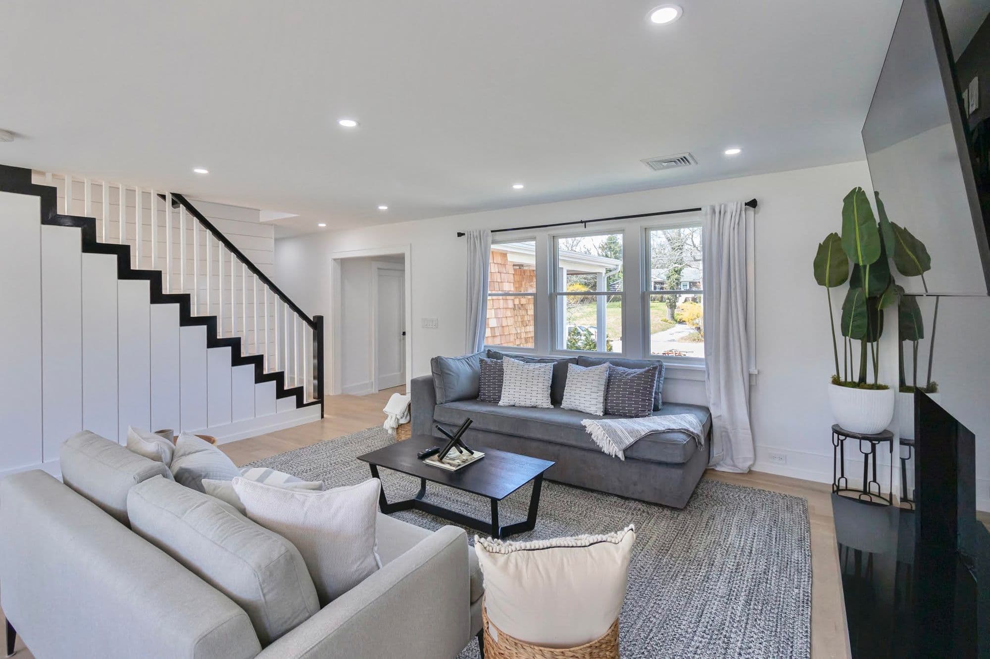 Wide-angle view of living room with white shiplap staircase, dual sofas, and cedar shingle exterior