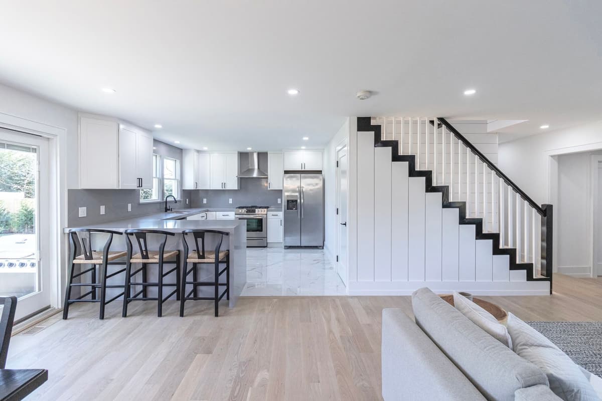 Modern kitchen with white painted cabinets, gray backsplash, island seating, and shiplap staircase