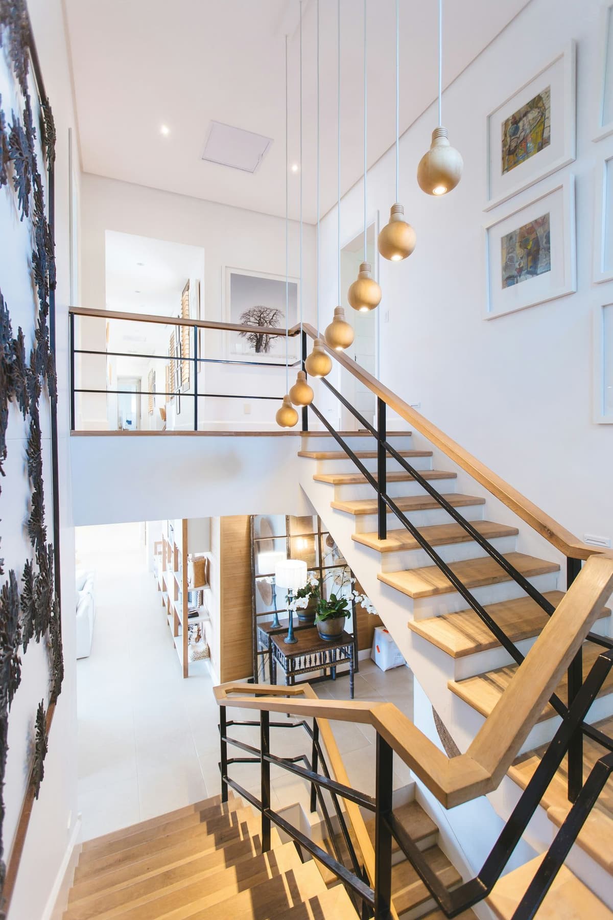 Multi-level staircase with oak treads, black metal railings, pendant globe lights, and gallery wall