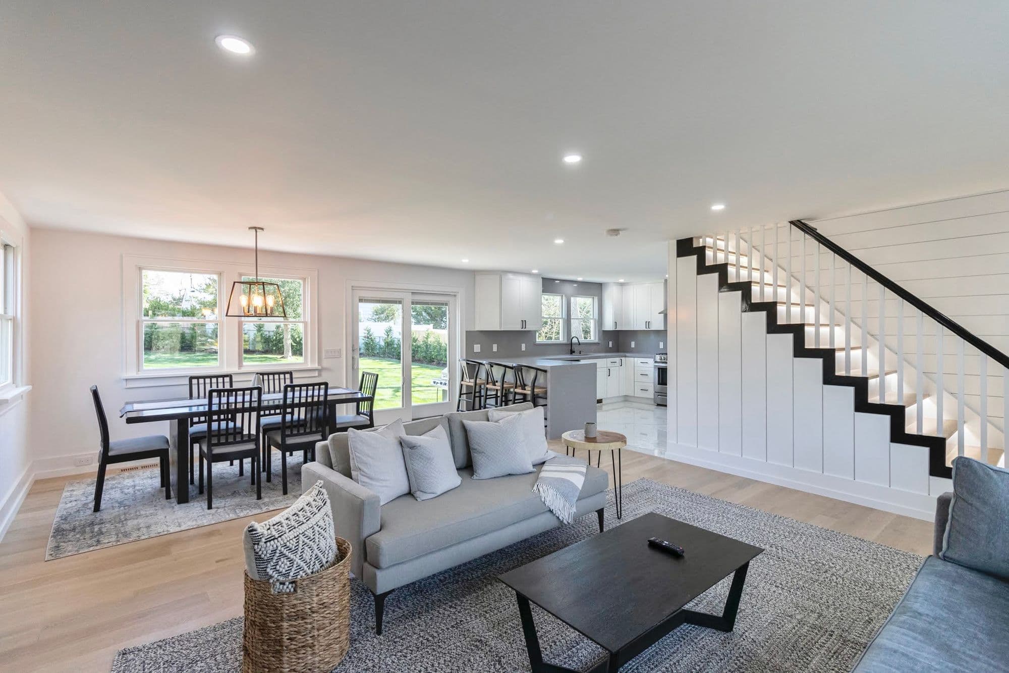 Open-concept living and dining area with white shiplap staircase, light hardwood floors, and garden views