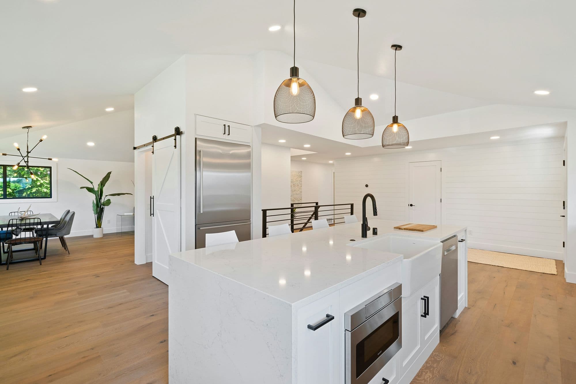 Open kitchen with vaulted ceiling, white quartz island, pendant lights, barn door, and shiplap walls