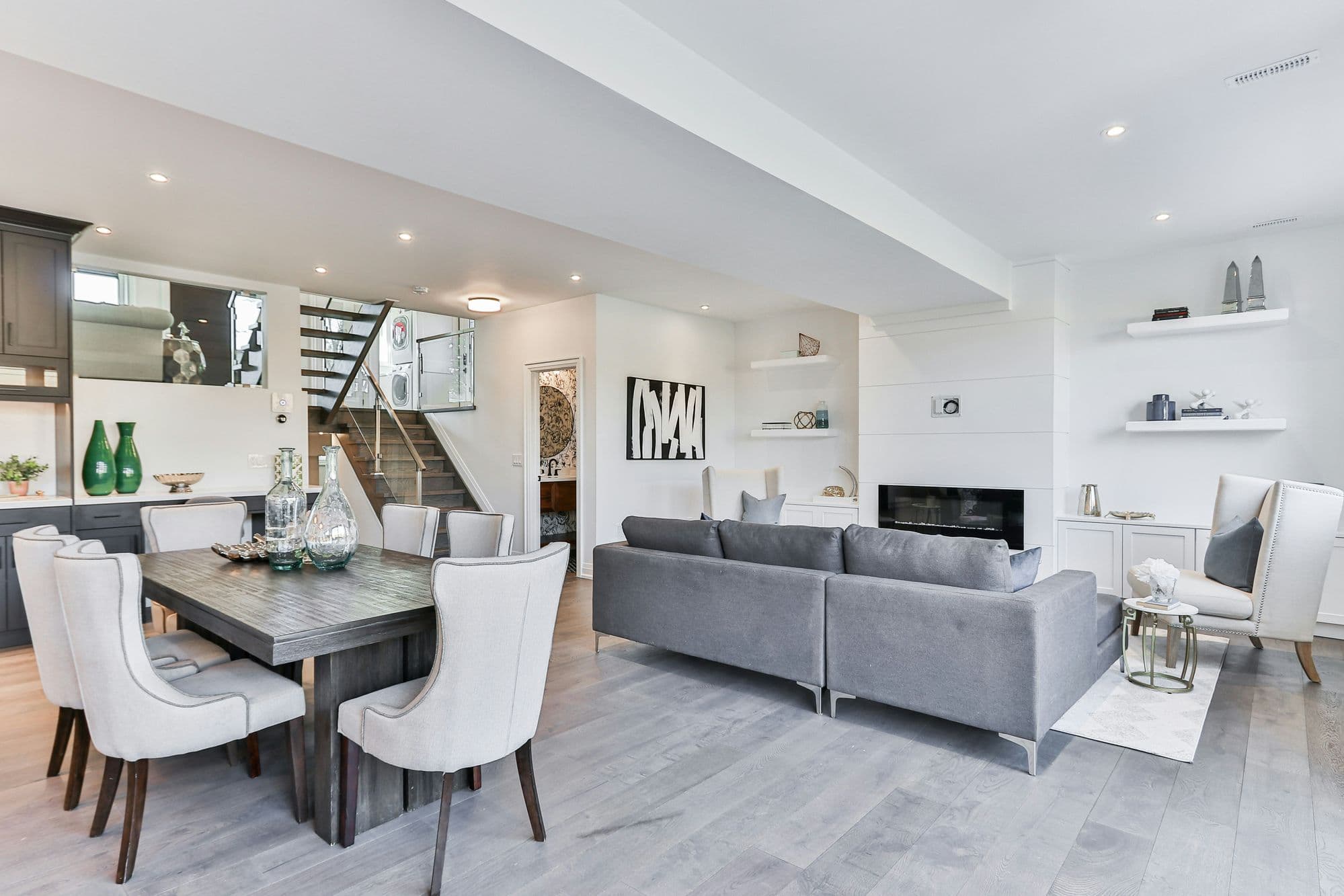 Open-concept living and dining area with gray sectional, white shiplap fireplace wall, and floating shelves