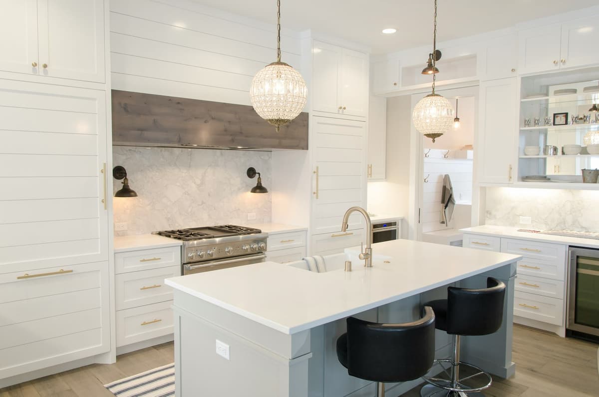 White shaker kitchen with marble backsplash, shiplap hood surround, crystal globe pendants, and island seating
