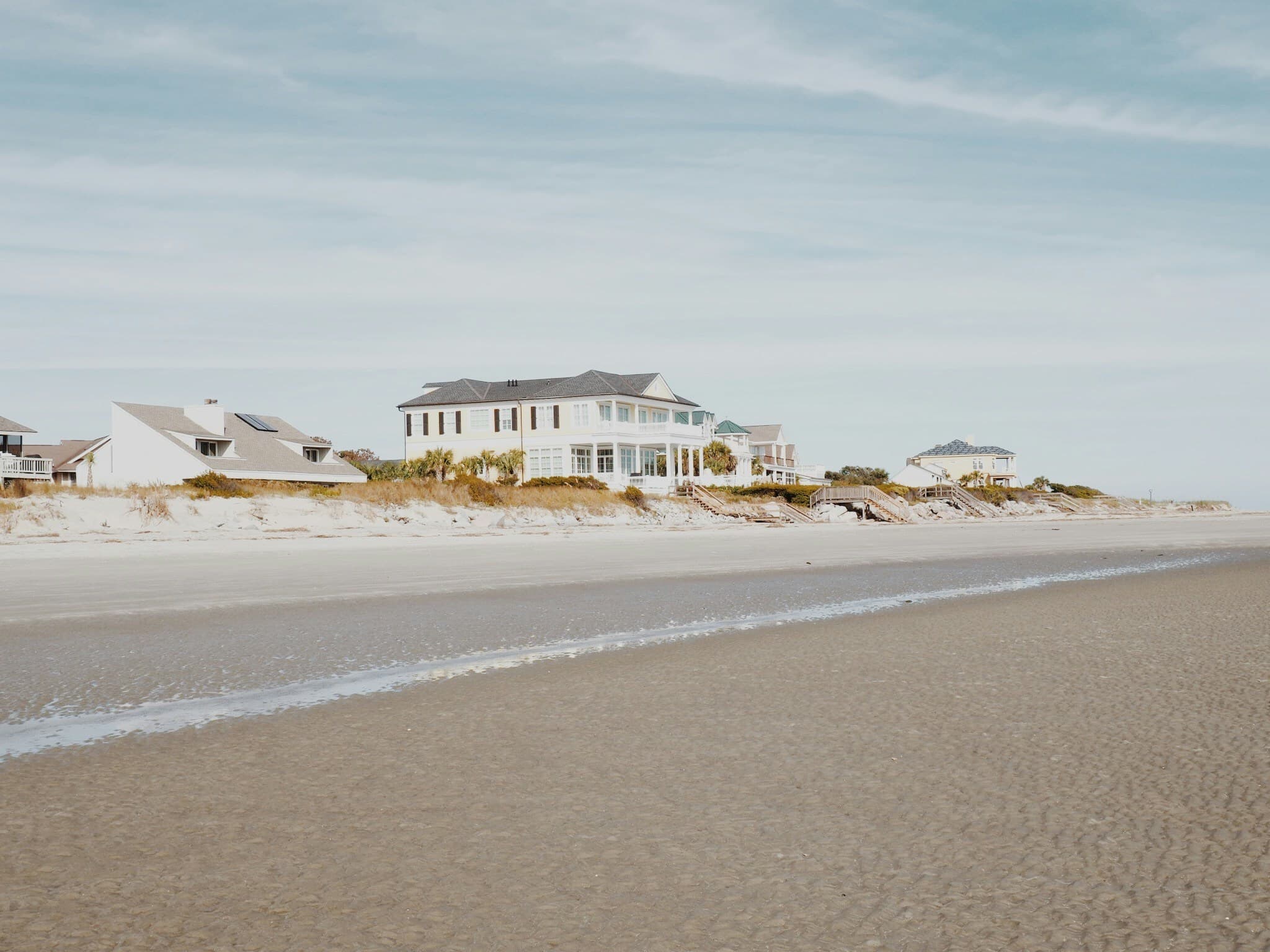 Beachfront Hamptons estates along the shoreline with pristine sand and coastal sky